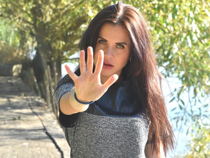 Fikitive Fallbeispiele aus Weimar und Merseburg Frau mit langen Haaren streckt die Hand aus, lächelnd in der Natur stehend.