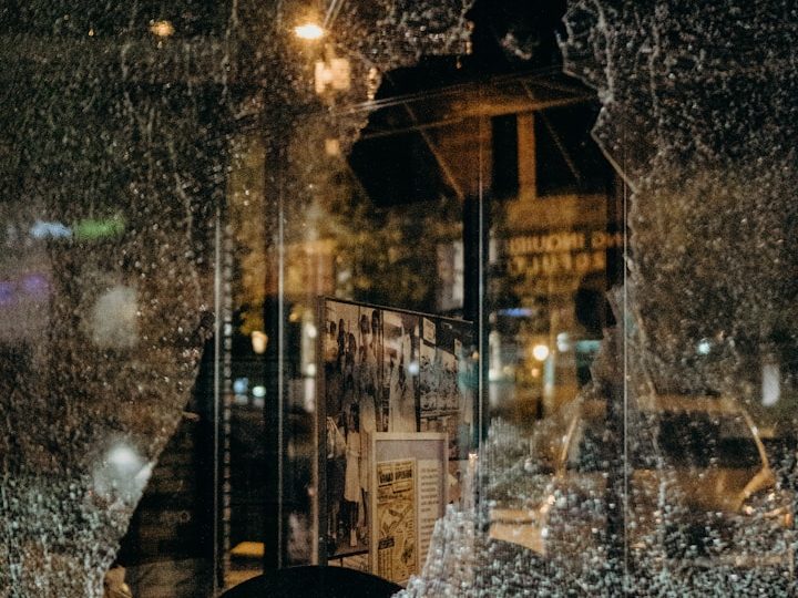Fikitive Fallbeispiele aus Oschatz und Plauen Zerbrochenes Fenster mit Rissen, im Hintergrund unscharfe Lichter und Straßenansicht.